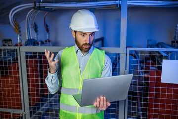 Caucasian factory worker in white hard hat and green safety vest hold laptop looking confused or angry