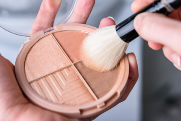 Woman's hands holding palette of blush for face and brush.