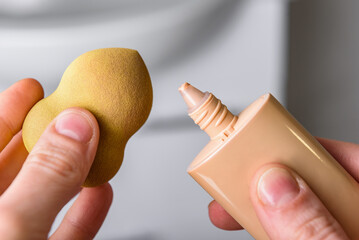 Young girl's hand holding tube with foundation and cosmetic sponge.