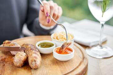 A piece of sausage is dipped in sauce. Lunch in a restaurant, a woman cuts Grilled sausages....