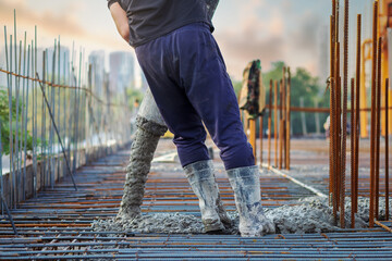 A construction site worker in rubber boots manipulates a concrete pump hose during the process of pouring concrete into a reinforcement cage. - obrazy, fototapety, plakaty