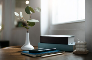 White vase with small tree inside on wooden table by the window, smart phone put on blue note book...
