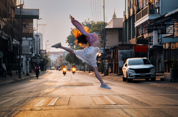 A joyful woman jumping high in the middle of an empty street at sunrise, symbolizing freedom and...