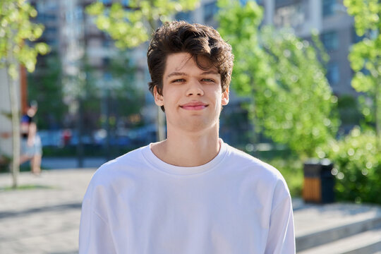 Headshot portrait of handsome guy 19, 20 years old, looking at camera outdoors