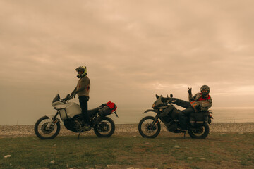 Bikers friends in motorcycle trip on adventure enduro motorcycles resting on sea shore