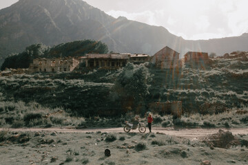 Female biker taking photo of her motorcycle trip on drone in Abandoned village in mountains. Beautiful mountain landscape at sunset, green spring slopes