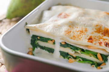 Front view of spinach lasagna, pine nuts and pear on oven tray