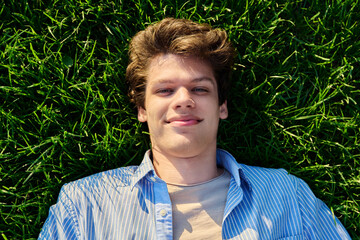 Top view, happy young male looking at camera, lying on green grass
