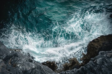 Fototapeta premium A view from a cliff of the ocean meeting the coastline, showcasing intricate patterns and textures of the water and rocks below