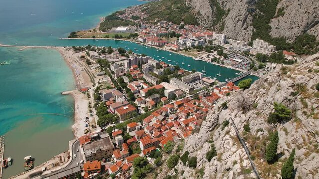 Aerial view of river Centina confluence with sea by town Omis in Croatia. Vessels navigate water channel. Seascape and urban life from above.