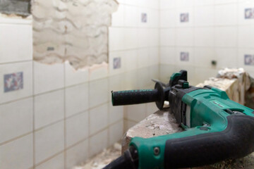 A construction worker is using a power tool to remove tiles from a bathroom wall.