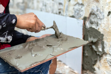 A construction worker is using a trowel to spread mortar on a wall.