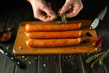 The cook adds aromatic rosemary to the smoked sausages with his hands. Low key concept of grilling...