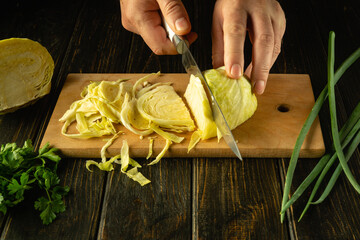 Close-up of a chef hands cutting fresh cabbage with a knife on a cutting board for preparing a...