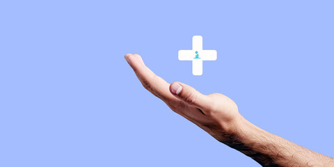 Male hand holding plus sign on blue background. Health care concept.