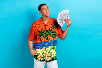 Photo of positive dreamy guy dressed print shirt air blowing cash fan isolated blue color background