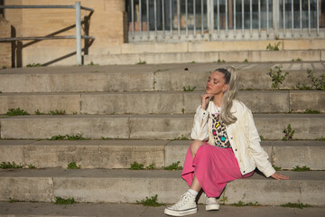 Young, pretty, blonde woman, with eyes closed, white fringed jacket and pink skirt, with her hand...