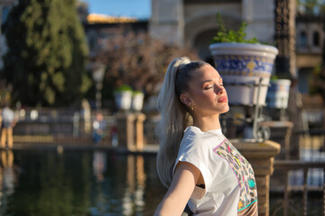 Young, pretty, blonde woman, with her eyes closed and a printed T-shirt, leaning against a railing,...