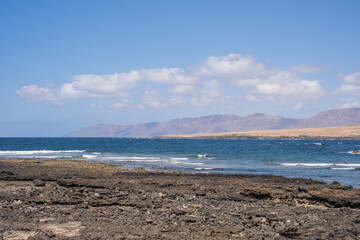 Seascape of the village of Caleta de Caballo, cliff and mountains of Famara in the background. Desertic landscape and ocean breaking against the rocks. Lanzarote, Canary Islands, Spain