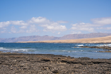 Seascape of the village of Caleta de Caballo, cliff and mountains of Famara in the background. Desertic landscape and ocean breaking against the rocks. Lanzarote, Canary Islands, Spain
