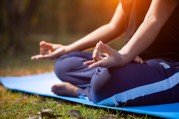 closeup view of an women practicing Apana Mudra hand gesture sitting on a exercise mat at outdoor