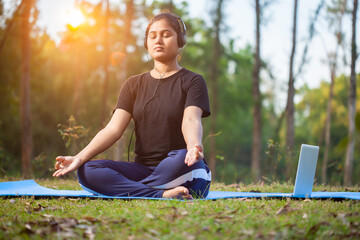 yoga women sitting in a padmasana or lotus position using laptop and headphone