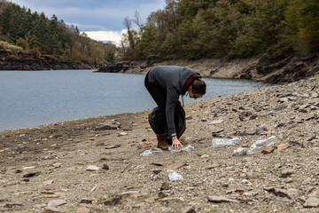 Young female volunteer activist litter picks at local beauty spot to care for the environment;...