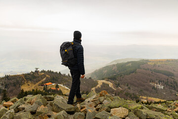 A male hiker steps over rocks on a hill top on a winter day with fog and some snow on the hills; a...