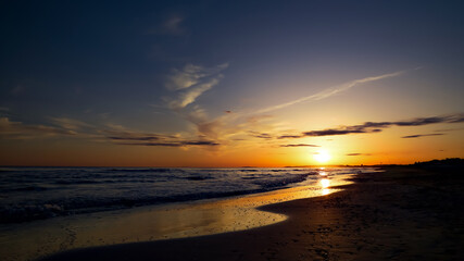 Beautiful sunset over a tranquil Mediterranean beach with golden sun reflected in shallow sea and...