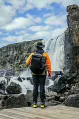 Oxararfoss, spectacular Icelandic waterfall. Þingvellir National Park. Cold water falls on large black boulders of volcanic origin. Hiker seen from behind standing at the waterfall.