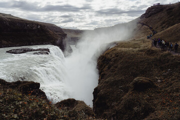 Gullfoss waterfalls in Iceland. Cold fog rises from the river bed. Water falls 32 meters. Breathtaking panorama. Queue of tourists in the distance.