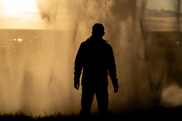 Person in silhouette under a huge waterfall. Hiker posing at sunset behind the Seljalandsfoss waterfall.