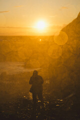 Hiker in silhouette at sunset. Halos on the lens, water, vapors, sprays, water drops. Dramatic light, travel, adventure.