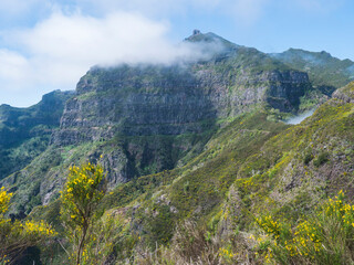 View of green hills, mountain landscape in clouds at blue sky. and lush vegetation at hiking trail PR12 to Pico Grande one of the highest peaks in the Madeira, Portugal