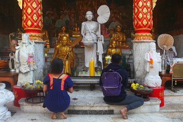 Chang Mai, Thailand, a couple of believers pray in front of golden statues of monks at the temple...