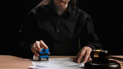 Female sitting at the desk with wooden hammer, dark room bright spotlight. Woman judge silhouette...