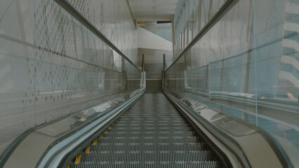 The photo shows an empty escalator going up. The escalator is made of metal and has a gray floor....