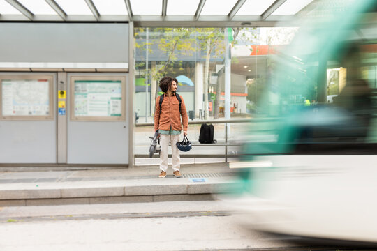 Man waiting at bus stop holding an electric scooter and a helmet