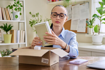 Female customer sitting at home unpacking cardboard box with online purchases