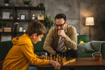 Father and son play chess together at home