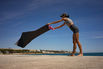 Athletic Brunette Woman Elegantly Unfolds Pink Exercise Mat on Seashore by the Ocean