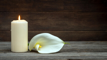 LIGHTED CANDLE AND CALLA FLOWER ON WOODEN BACKGROUND. DEAD DAY, FUNERAL, ALL SOULS DAY. COPY SPACE.	