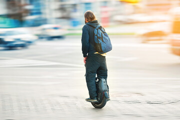 Man on electric unicycle riding fast along city street, motion blur. Mobile portable individual transportation vehicle. Man commuting to work on electric monowheel (EUC).