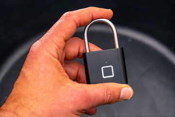 Black biometric padlock with fingerprint secure in hand. Black biometric padlock with fingerprint opening via square sensor held in hand