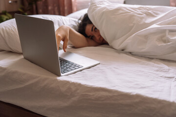 Lady working remotely while lying in bed with laptop.