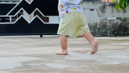 foot of child and mother walking in the park. Child learns to take the first steps in the park. close up leg of infant baby walking on path with mother helping