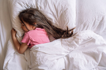 Little girl in pink pajamas sleeps in white bed linen.