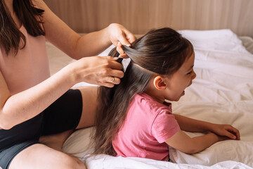 Mom braids her daughter's hair while sitting in bed.
