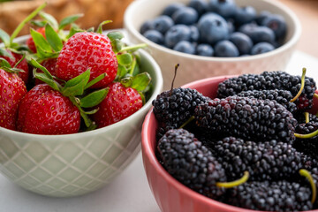Closeup view of blueberries, strawberries and black mulberries in bow