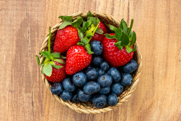 Top view of blueberries and strawberries in wicker bowl on wooden table
